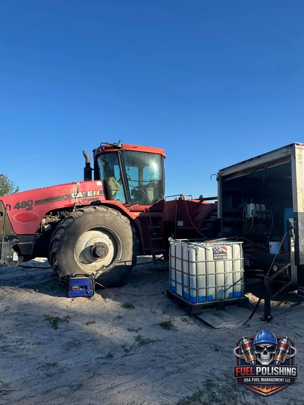 A red tractor beside a mobile service vehicle, hoses and a collection tote